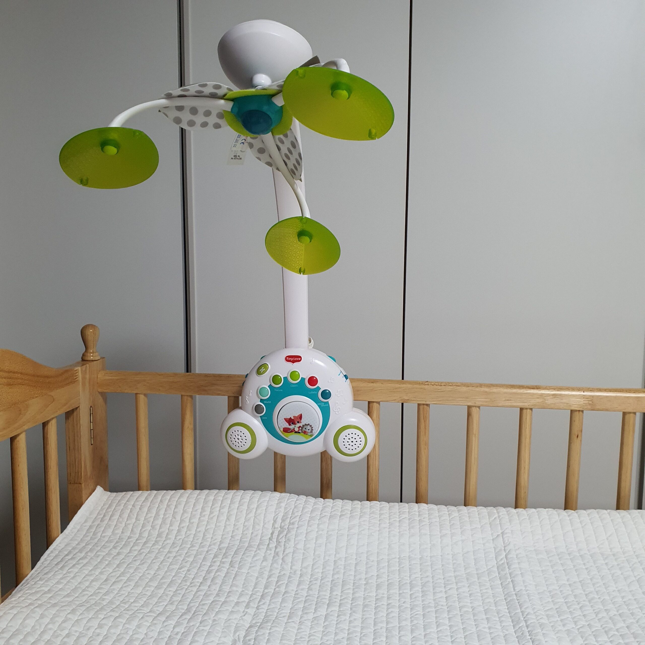 아기 침대 위에 흰색 순면 이불이 깔려있고 모빌이 설치되어 있다
