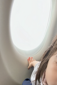 비행기 안에 앉아있는 아기의 볼과 손, 비행기 창문이 보인다